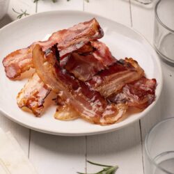 Crispy cooked bacon strips on a white plate with a rustic kitchen background.