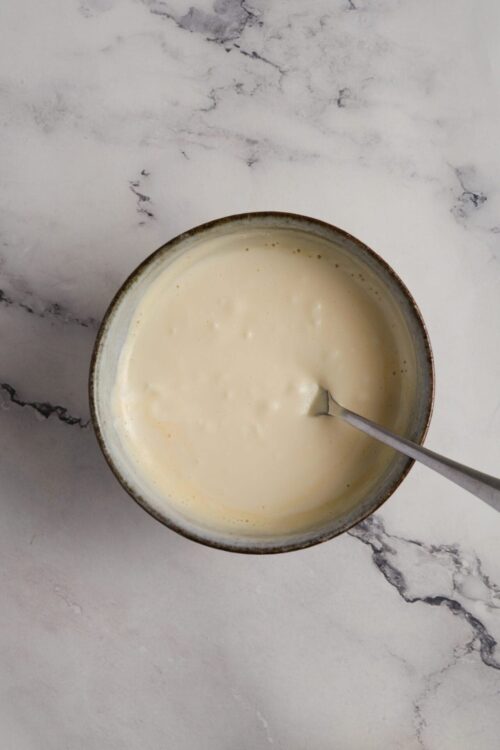 Creamy custard mixture in a rustic bowl on marble surface.
