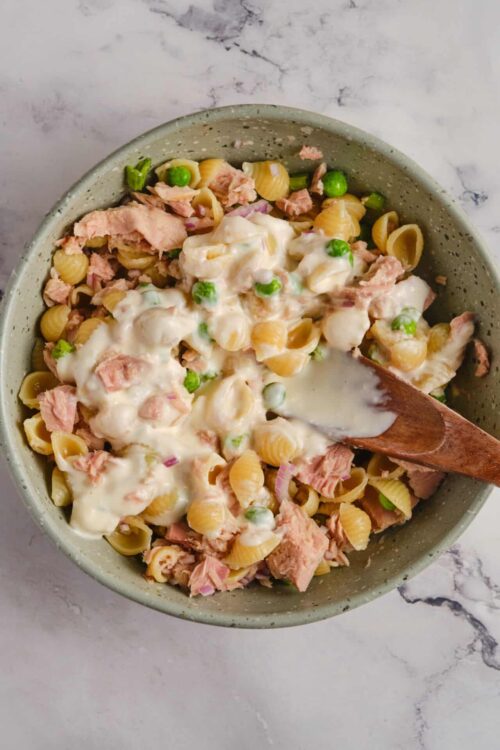 Creamy tuna pasta salad with peas and red onions in a ceramic bowl on marble surface.