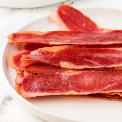 Crispy bacon strips on white plate, fresh and savory breakfast bacon.