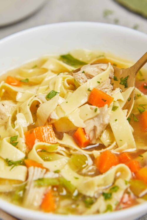 Creamy chicken noodle soup with carrots and celery in a white bowl, garnished with herbs.