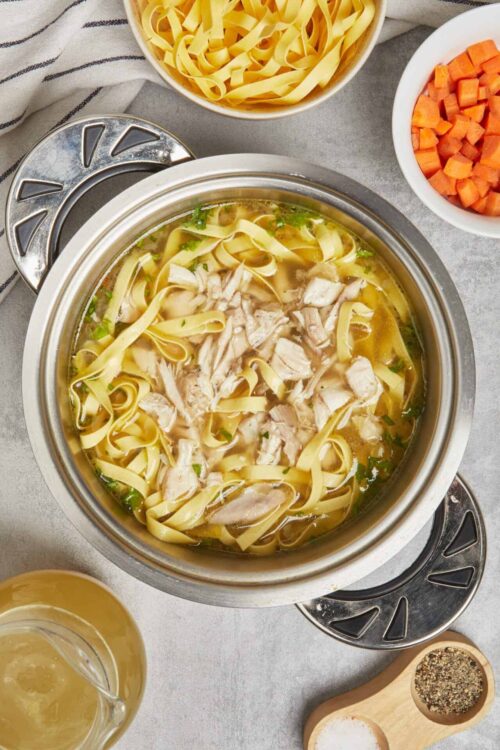 Steamy chicken noodle soup with shredded chicken, egg noodles, and fresh vegetables in a pot.
