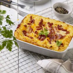 Cheddar bacon potato casserole baked in a white dish, garnished with fresh parsley.