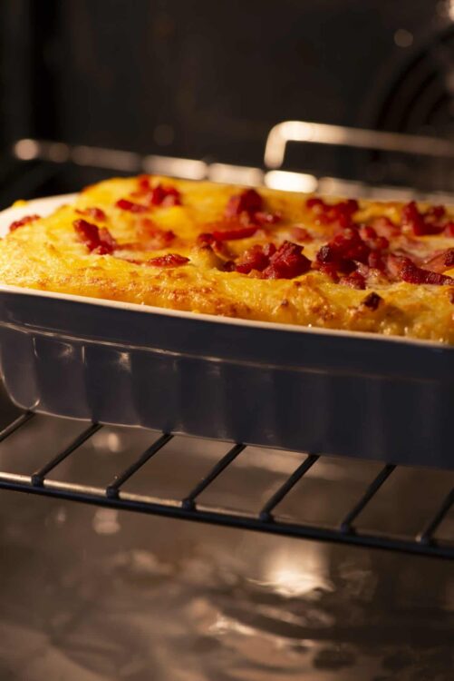 Golden baked casserole with crispy bacon pieces in oven.