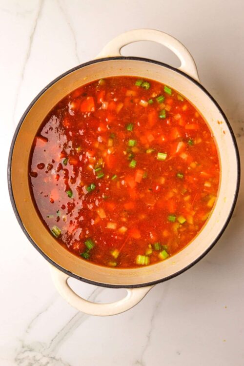 Savory homemade vegetable soup in a white enamel pot on white marble surface.
