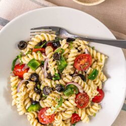 Vegan pasta salad with cherry tomatoes, olives, green peppers, and red onions on a white plate.