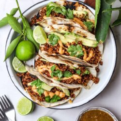 Fresh grilled fish tacos with quinoa, avocado, cilantro, and spicy sauce garnished with lime wedges.