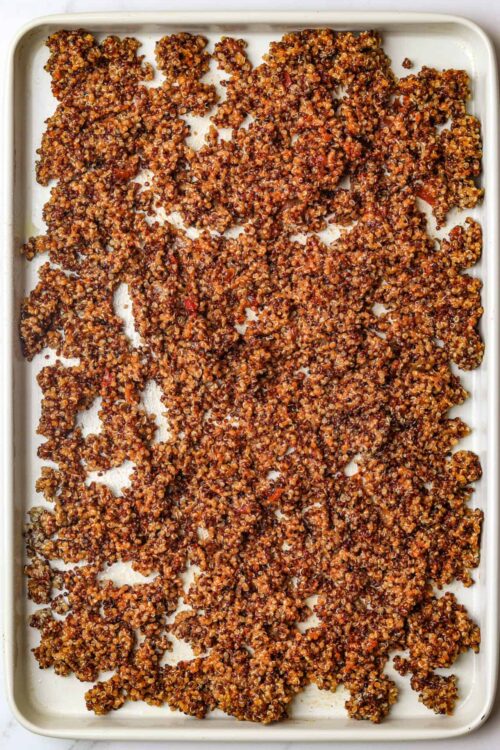 Crispy baked quinoa granola clusters on a white baking sheet.