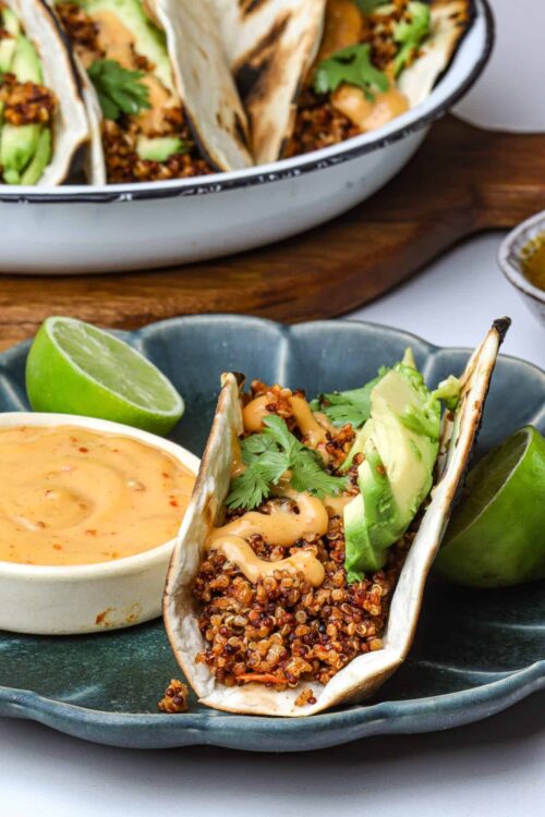 Crispy lentil taco with avocado and cilantro, served with creamy sauce and lime wedges.
