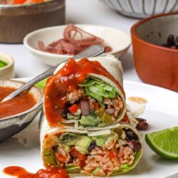 Fresh vegetarian rice burrito sliced in half with beans, vegetables, and salsa on a white plate.