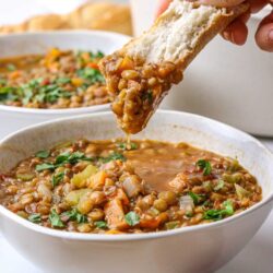 Creamy lentil vegetable soup served with a slice of bread for dipping.