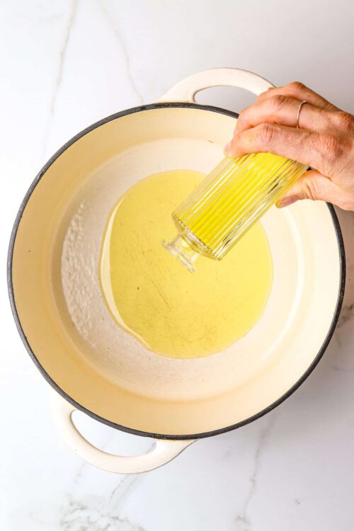Creamy yellow sauce being poured into a pot from a glass jar.