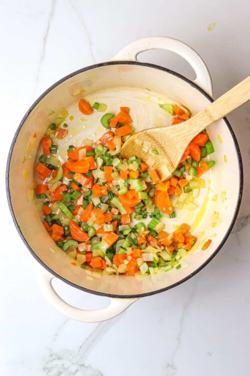 Chopped vegetables in a white enamel pot on marble surface, prepared for baking or cooking.