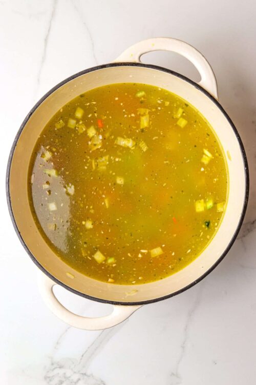 Savory homemade vegetable broth in a pot on a marble countertop.