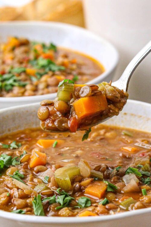 Hearty vegetable lentil soup with carrots, celery, and herbs in a white bowl.