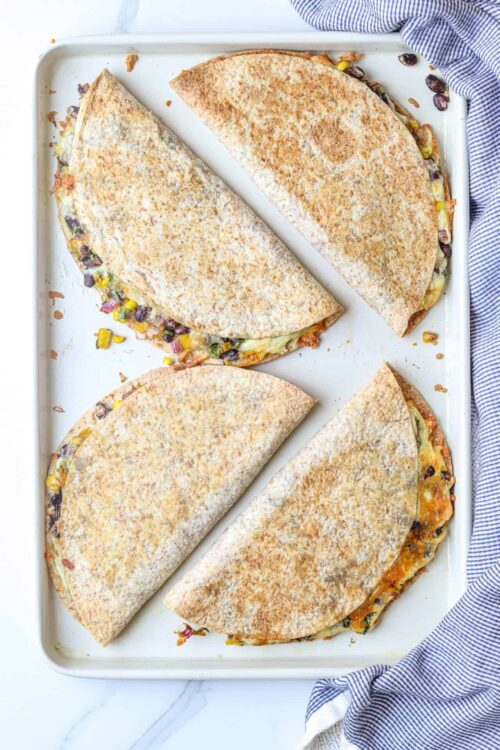 Stuffed calzones with cheese, beans, and vegetables on baking sheet.