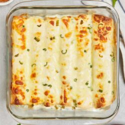 Cheesy baked enchiladas in a glass casserole dish with green onions and melted cheese.