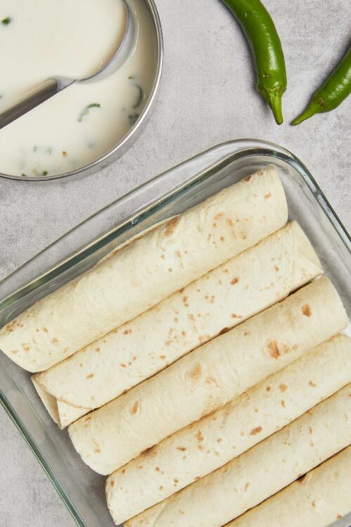 Golden brown flour tortillas stacked in a glass baking dish on a kitchen counter, ready to be baked or cooked.