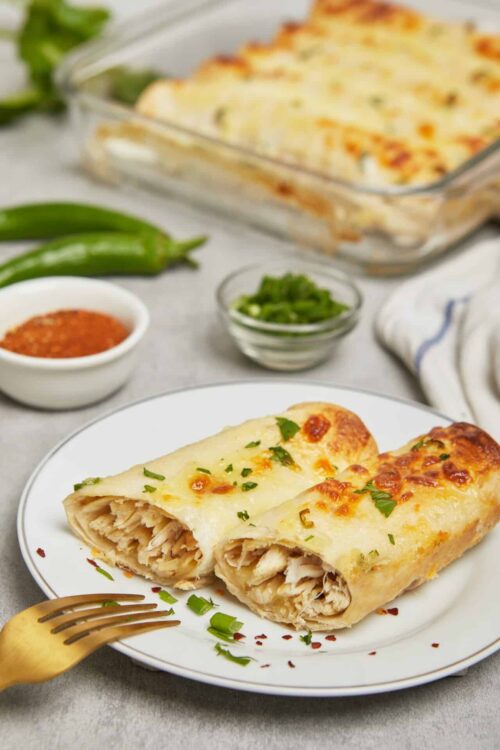Baked chicken chimichanga with melted cheese and fresh herbs on white plate.