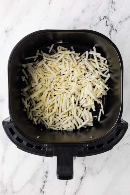 Shredded cheese in an air fryer basket for cooking or melting purposes.