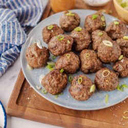 Juicy homemade meatballs garnished with sliced green onions on a blue plate.