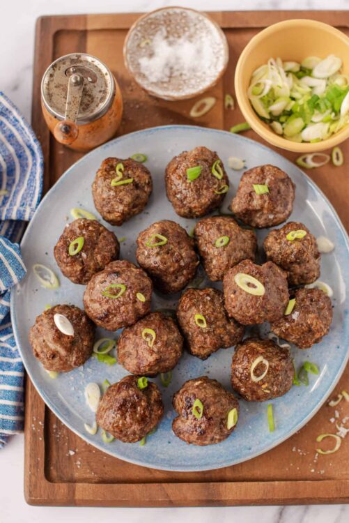 Savory homemade meatballs with chopped green onions on a ceramic platter.
