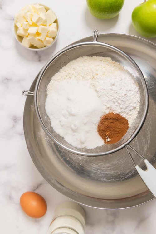 Flour, sugar, cinnamon, and butter in a sifter on a mixing bowl for baking.
