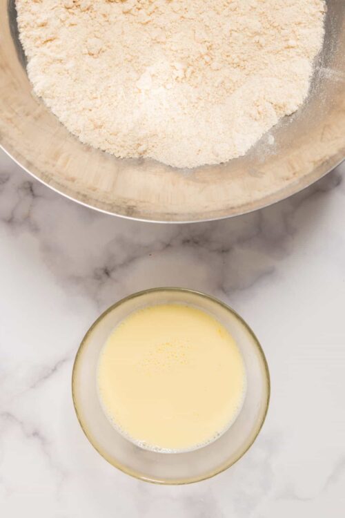 Flour and eggs on marble countertop for baking bread or pastry preparation.