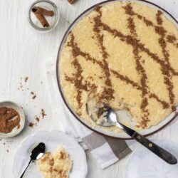 Rich creamy banana pudding dessert topped with vanilla wafers and sprinkled with cinnamon, served in a glass dish.