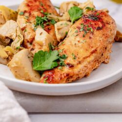 Juicy roasted chicken breast with herbs and potatoes on a white plate.