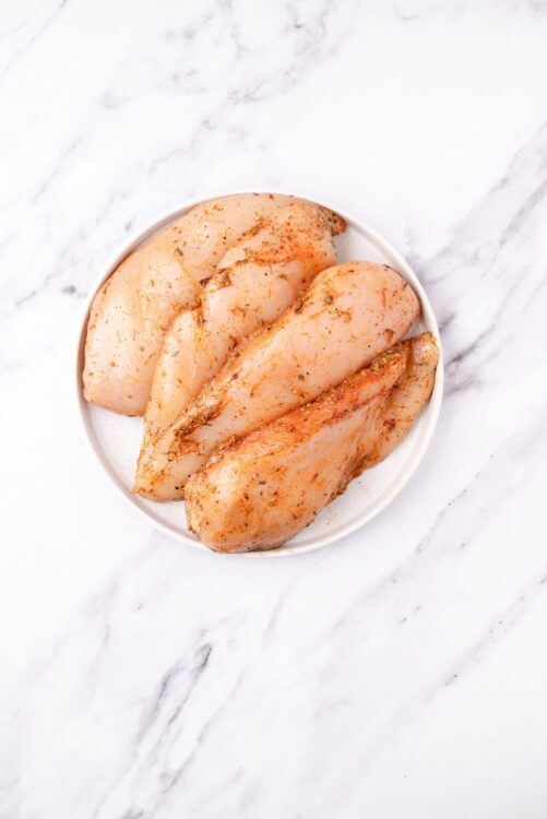 Marinated chicken breasts on white dish, ready for cooking or baking.
