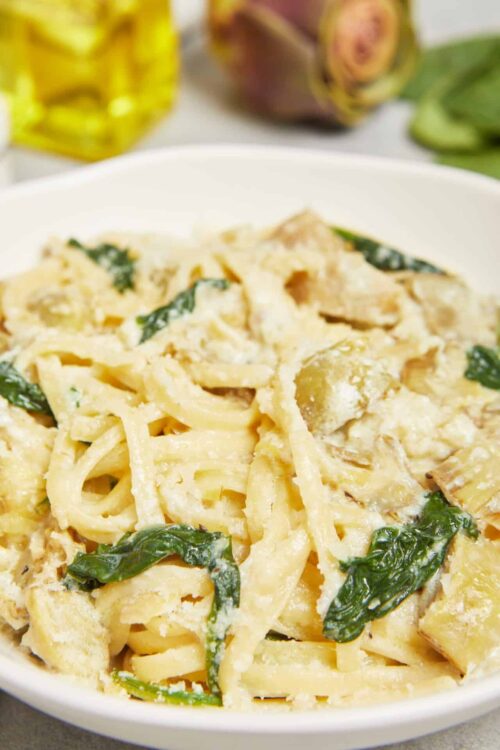 Creamy fettuccine alfredo with spinach and chicken in a white bowl. Perfect comfort food recipe for dinner or entertaining guests.