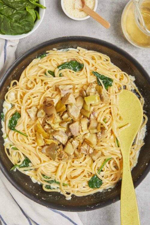 Creamy chicken and spinach pasta dish with artichokes in a skillet, garnished with fresh herbs.