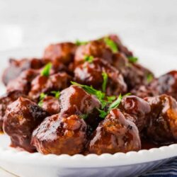 Succulent homemade meatballs in rich tomato sauce garnished with fresh herbs on a white platter.