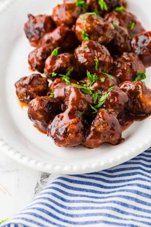 Crispy glazed beef meatballs garnished with fresh herbs on white plate.