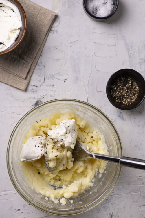 Creamy mashed potatoes with butter and black pepper in a glass bowl.