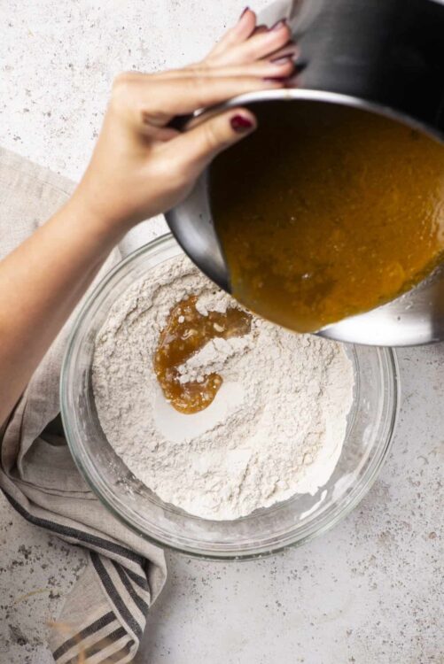 Butterscotch sauce being poured into a bowl of flour and baking ingredients.