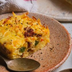 Creamy breakfast casserole with cheese, bacon, and vegetables on a speckled ceramic plate.