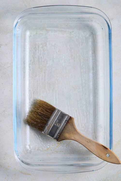 Empty glass baking dish with a paintbrush inside, ready for baking or kitchen prep.