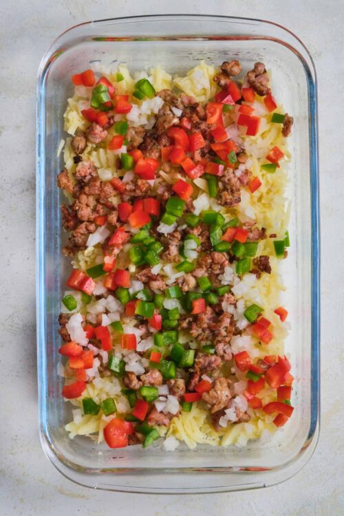 Cooked ground beef and vegetable casserole with diced red and green bell peppers and onions in glass dish.