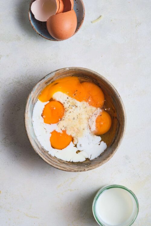 Eggs in a rustic bowl with milk and eggshells on a kitchen countertop, ideal for baking and breakfast recipes.