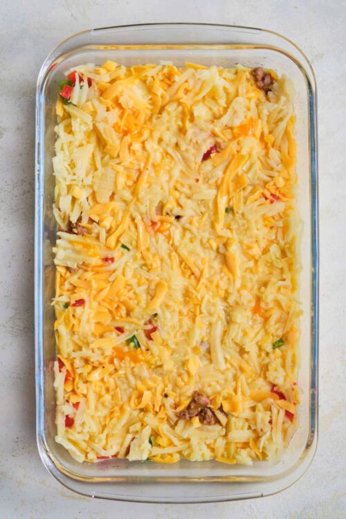 Baked cheesy casserole with melted cheese, ground beef, and colorful vegetables in a glass dish.