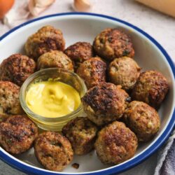 Savory meatballs with mustard sauce in a white bowl, close-up.
