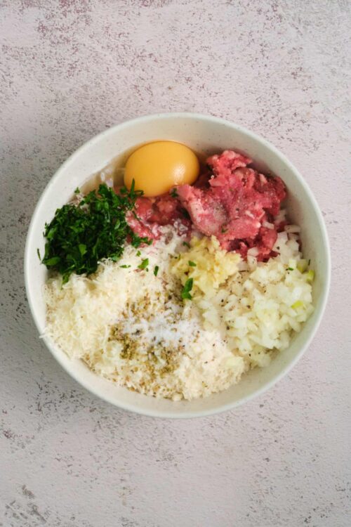 Eggs, chopped onions, cheese, and herbs in a white bowl for baking or cooking.