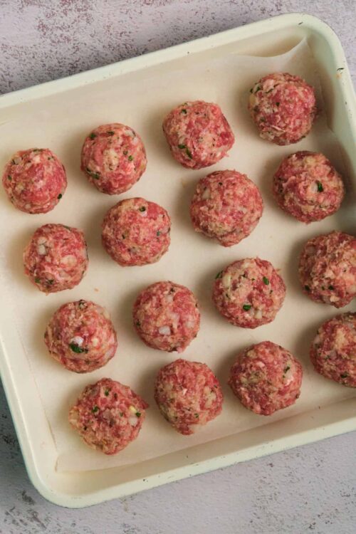 Raw homemade meatballs with herbs in a baking dish.