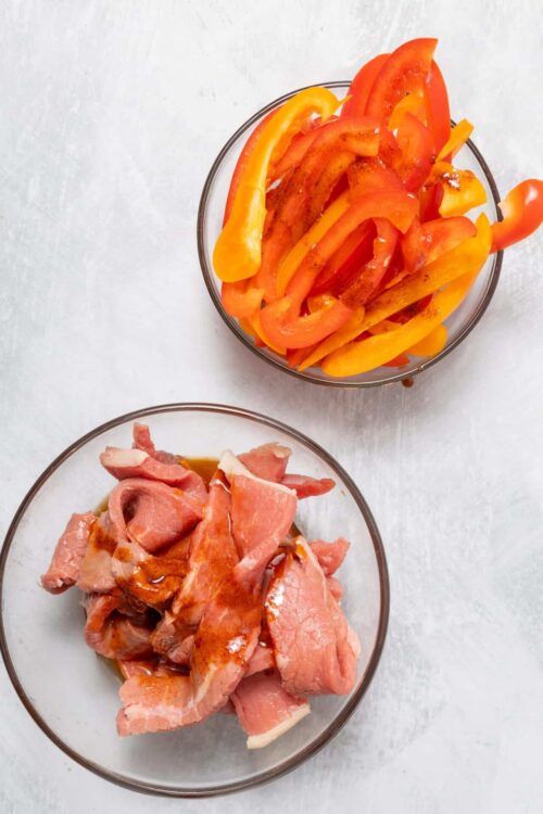 Sliced colorful bell peppers and raw chicken in glass bowls for cooking or meal prep.