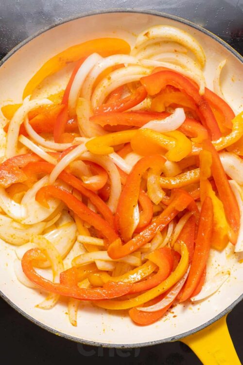 Sautéed colorful bell peppers and onions in a white pan, ready for a delicious recipe.