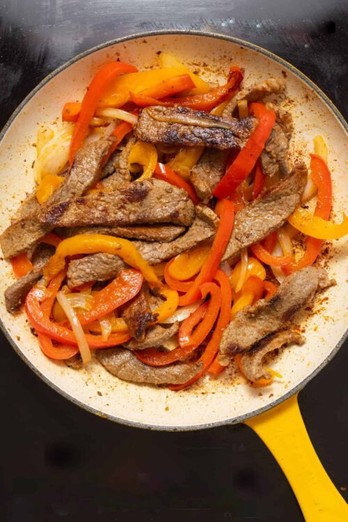 Sautéed beef and bell peppers in a white skillet with a yellow handle, cooked to perfection.