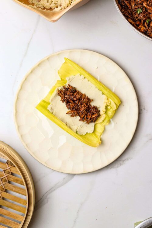 Cream cheese-filled celery stalk with pulled pork topping, on a white marble surface.