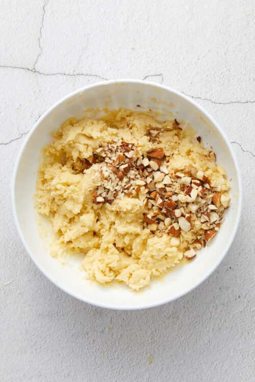 Creamy cookie dough with chopped almonds in a white bowl on a textured surface.